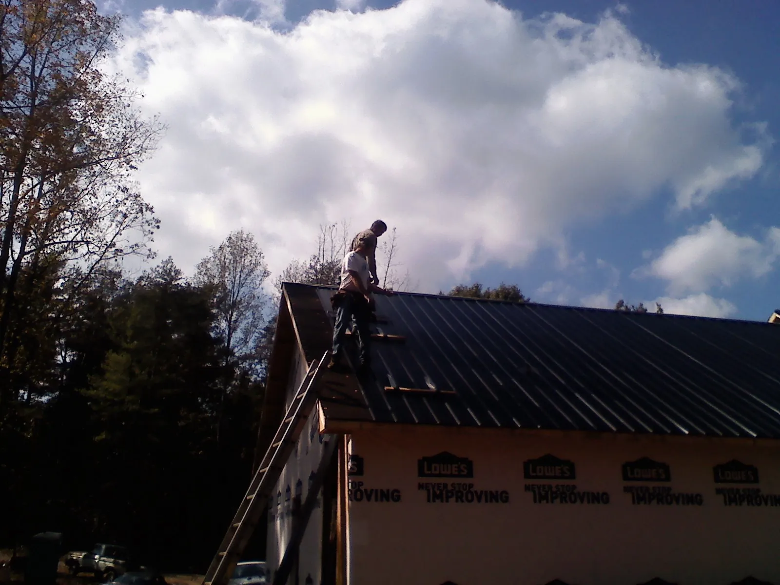 Roofer fastening dark metal panels high against a cloudy sky, from a Roof Inspection job in Spring Valley