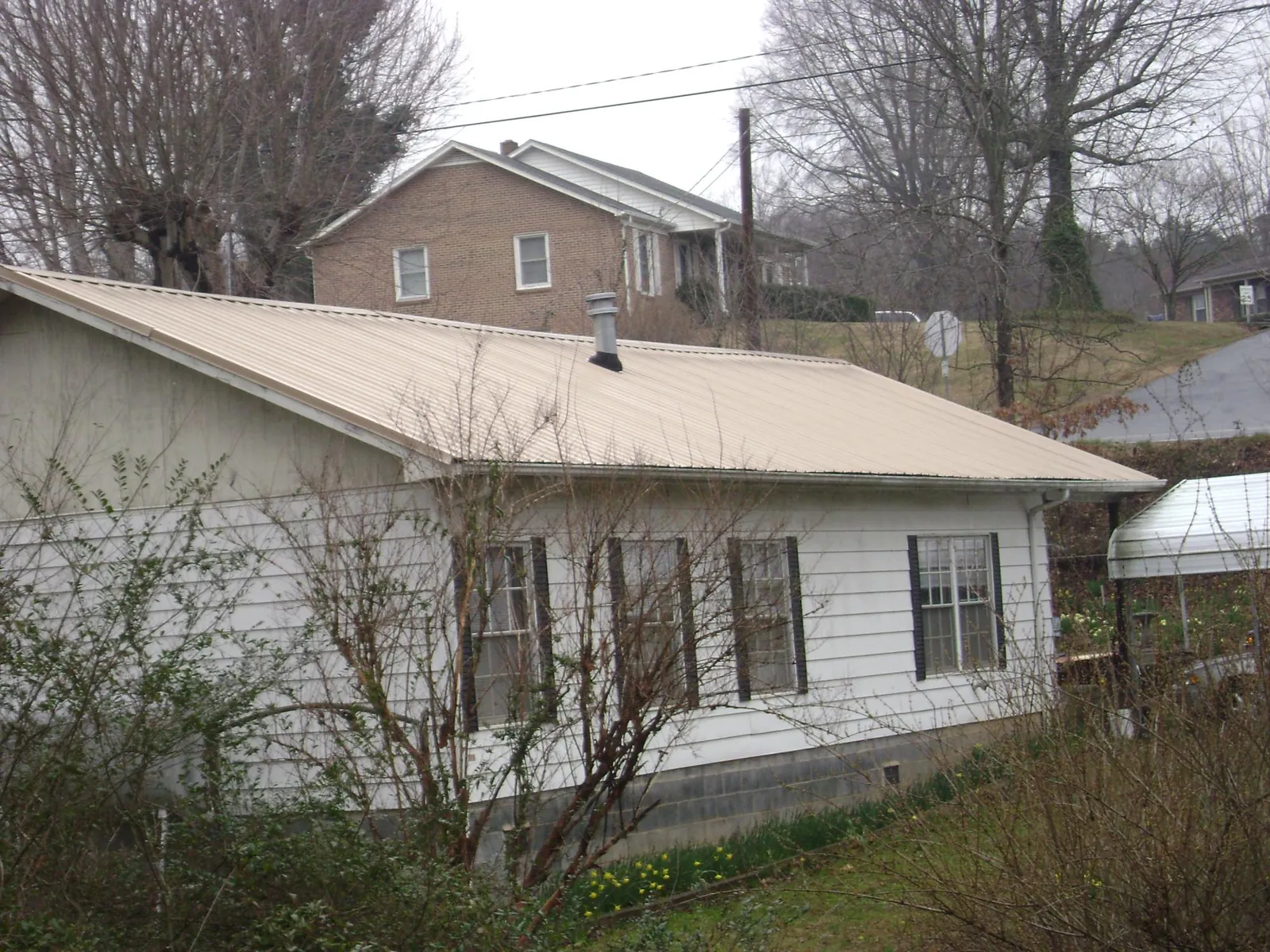 Tan metal roof on a white sided house set into a hillside — Commercial Roofing by Roofing Brothers in Spring Valley